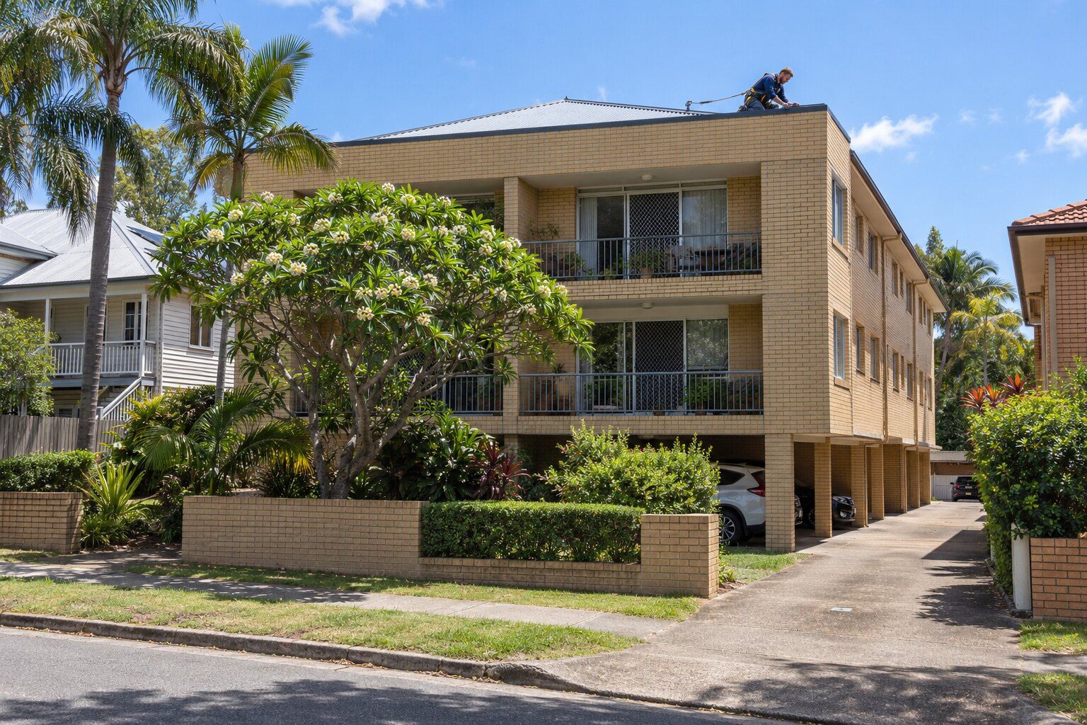Body corporate roof repairs, Brisbane: roofer checking a box gutter outlet on the roof of a 1970s brick block of units
